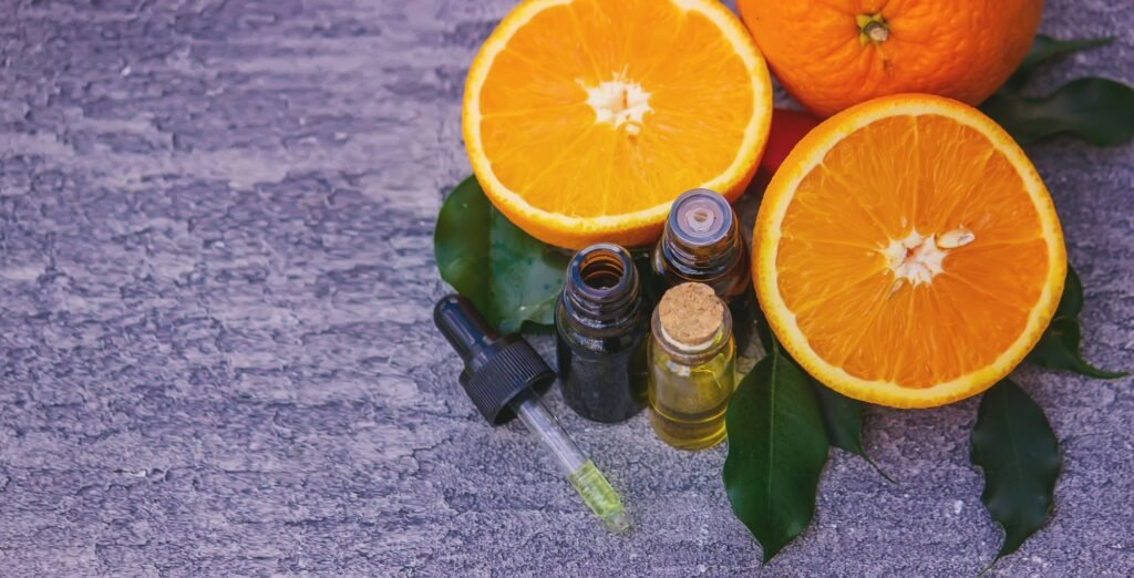 Essential orange oil in a bottle, fresh fruit pieces on the background.